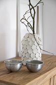 Branch in vase hand-made from preserving jar and modelling compound discs behind two bowls