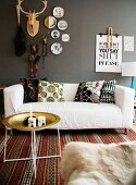 Tabletttisch, weisses Sofa mit gemusterten Kissen und Webteppich vor grauer Wand mit Dekorationen