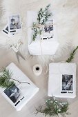 White-wrapped Christmas gifts decorated with evergreen sprigs and photos