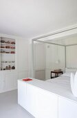 Doppelbett mit Baldachingestell und weißem Sideboard am Fussende, Kassettenwände und Kunstobjekte auf integrierten weißen Regalbrettern