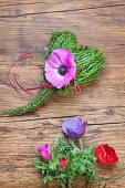 Frühlingsgesteck aus Heiderlbeerstengeln in Herzform und violette Anemonenblüte