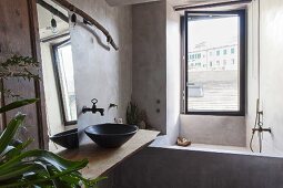 Renoviertes Bad mit betonierter Badewanne vor Fenster und schwarzer Waschschüssel auf Vintage-Holzbrett
