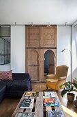 Bücher auf rustikalem Palettentisch und Armlehnsessel im Wohnbereich vor marokkanischen, verzierten Holzelementen