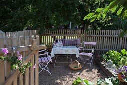 Romantic seating area in front of picket fence and deciduous trees in garden