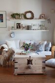 Comfortable wicker sofa below elegant floating shelves and vase of mallows on rustic trunk table