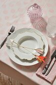 An elegant porcelain place setting with decorative arrows on a pastel pink spotted tablecloth