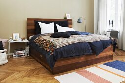Elegant wooden bed with integrated storage drawer on herringbone parquet floor