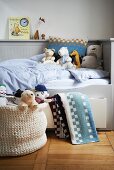 Kinderbett mit hellgrauer Holzverkleidung, Bettschublade und Kuscheltieren