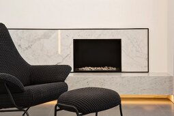 Elegant, modern, marble-clad fireplace with indirect lighting and designer armchair