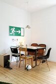 Simple dining area with various chairs and emergency exit sign on wall in corner of minimalist room with old, well-tended wooden floor