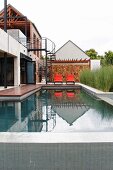 Modern house with pool, steel spiral staircase and orange loungers against stone wall