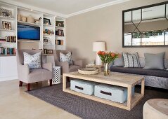 Comfortable living room with white fitted shelving, beige armchairs, wicker sofa and floor cushions on lower shelf of coffee table