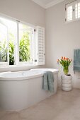 Free-standing bathtub in minimalist bathroom with white shutters and walls painted beige