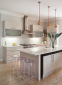 Pale, fitted kitchen with modern island counter and plexiglas bar stools