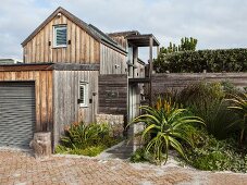 Weathered wooden house with attached garage, screen fence and flowering aloe next to entrance
