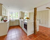 Open-plan country-house kitchen with rustic wooden columns, pale cupboards and terracotta floor tiles