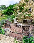 Wicker chairs and rustic wooden table in seating area on paved terrace next to flowering rose climbing over stone façade