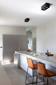 Barhocker mit lederbezogenen Sitzschalen vor Kücheninsel mit Betonarbeitsplatte in minimalistischer Küche