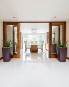 View from tiled foyer through open glass double doors flanked by planters into elegant dining area