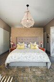 Double bed with button-tufted headboard and scatter cushions against partition and below chandelier in modern bedroom