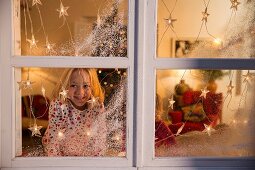 Girl looking out of window decorated with artificial snow and fairy lights