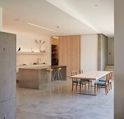 Open-plan designer kitchen with island counter, dining table and upholstered chairs in minimalist interior