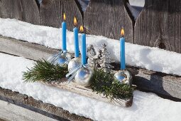 Advent arrangement of shiny baubles used as candle holders on snowy, weathered wooden surface