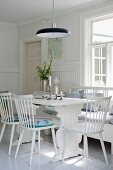 White wooden chairs and wooden table in dining area below black pendant lamps in Scandinavian interior