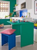 Kleines Appartement mit platzsparendem grünem Frühstückstisch, passender Wandfarbe und blauem Holzhocker
