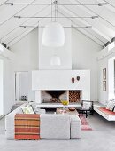 Exposed roof structure, pale grey corner couch, open fireplace and pendant lamps with white lampshades in white interior