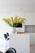 Vase of yellow flowers on white counter in fitted kitchen