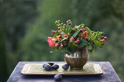 Autumn still-life arrangement with posy of berries in brass vase and plums on tray
