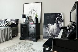 Schwarz-weisser Schlafraum mit Klavier, Kommode und Pferdefoto an Wand gelehnt