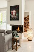 Fireplace, firewood store, rustic wooden side table and floor lantern on white wooden floor