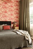 Blanket on double bed with headboard against wall with red and white toile de jouy wallpaper
