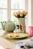Kuchenteller und Rosenstrauss neben Teekanne auf Tisch