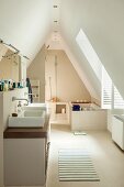 Spacious bathroom in converted attic; washstand with twin basins and bathtub under sloping ceiling