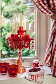 Red glass candelabra and tealight holders on windowsill with red gingham curtain