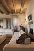 Elegante, weiße Sofagarnitur in Wohnzimmer mit Holzbalkendecke
