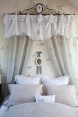 Romantisches Bett mit Spitzenkissen, an Wand transparenter Vorhang mit Schabracke