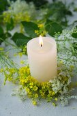 Lit pillar candle in wreath of rapeseed flowers and elderflowers
