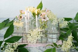Candles, elderflowers and blackberry blossom in glasses in metal basket