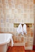 Bathtub next to towel hooks with shelf on wall with patterned wallpaper