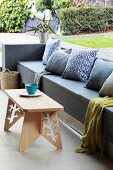Built-in grey bench with colour-coordinated cushions and wooden stool used as coffee table on terrace