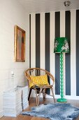 Rattan chair in corner of room against black and white striped wall and next to green retro standard lamp