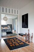 African sculpture and patterned rug on wooden floor in hallway leading to open sliding door with view into bedroom