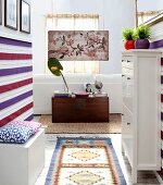Hallway and white shoe cabinet, striped wall hanging and wooden trunk below antique painting on wooden panel at far end