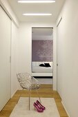 Femininer weißer Ankleidebereich mit Einbauschränken, edlem Metallstuhl und Blick in elegantes Schlafzimmer
