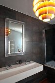 Modern bathroom with dark wall tiles, white designer sink with twin taps and retro pendant lamp