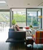 Sofa und Sessel um weissen Bodentisch in zeitgenössischem Wohnzimmer vor raumhoher Fensterfront